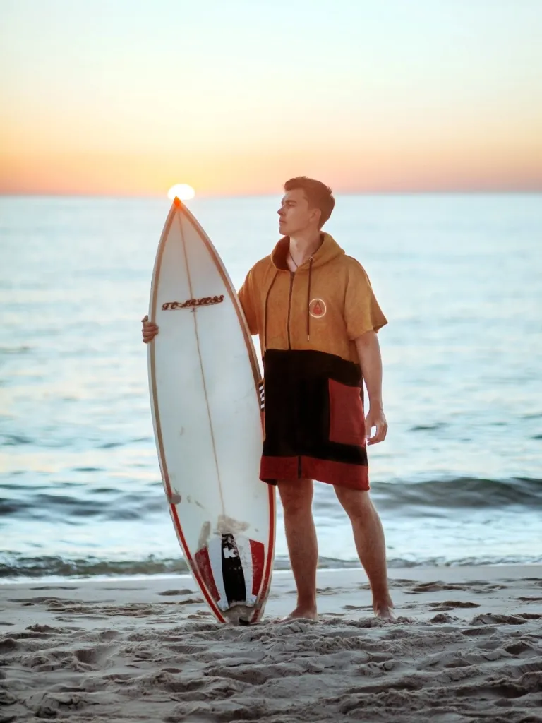 Barbat langa o placa de surf care poarta un poncho plaja dama colorat, pentru plaja, scuba sau surfing, culoare maro, negru si rosu