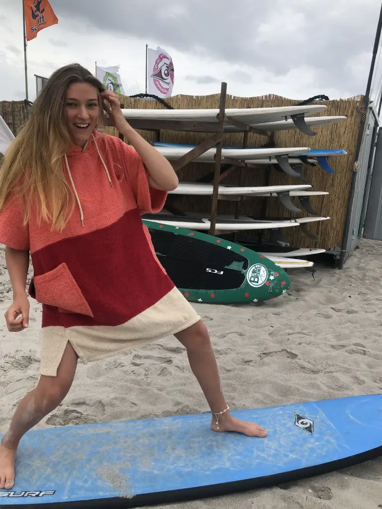 Femeie pe o placa de surf care poarta un poncho plaja dama din bumbac, culoare rosu deschis, rosu inchis, crem
