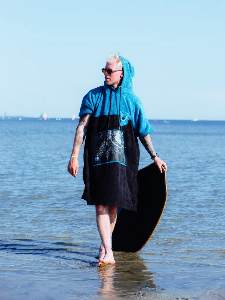 Barbat care poarta pe plaja un poncho barbati din bumbac si bambus organic, culoare albastru cu negru