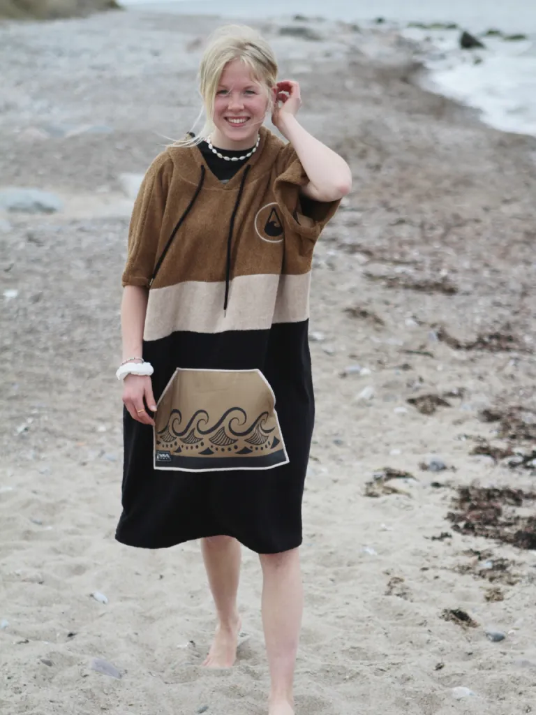 Pe o plaja, o femeie care poarta un poncho plaja dama colorat, culoare maro, negru si bej.